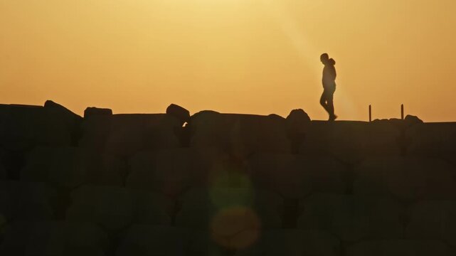 People Walking on Top of Coastal Defense Sea Wall Made with Concrete Blocks during Golden Hour Sunset