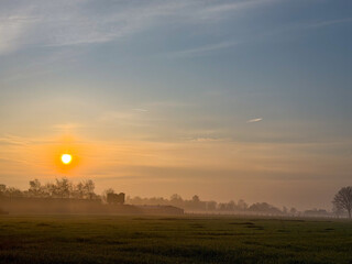 Fototapeta premium Golden sunrise over rural farmland with barn silhouette in misty countryside landscape