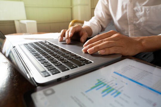 businessman working on laptop computer and closes on hands typing keyboard documents and paper charts financial on the desk. Business and technology concept.