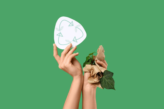 Female hands with recycle sign, plant and paper on green background. Ecology concept
