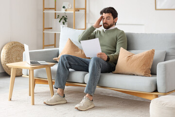 Fototapeta premium upset young man with order for his dismissal sitting on sofa at home