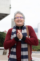 Senior man standing and clapping on outdoor terrace, wearing red sweater, striped scarf, eyeglasses © wavebreak3