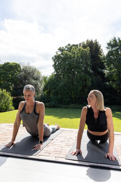 Senior and adult women practicing back-bend on black yoga mats on brick terrace, smartwatch visible