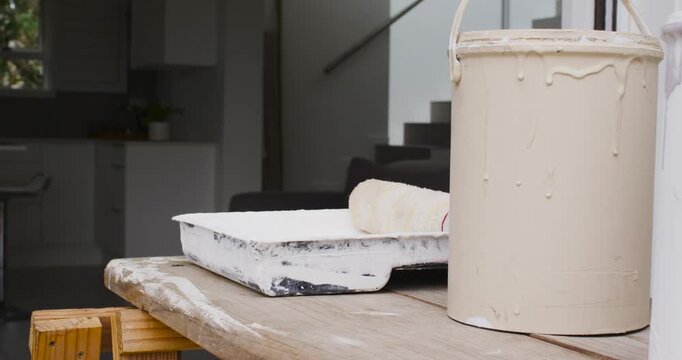 Camera panning slowly, revealing paint tray with roller, two cans on plank and kitchen window