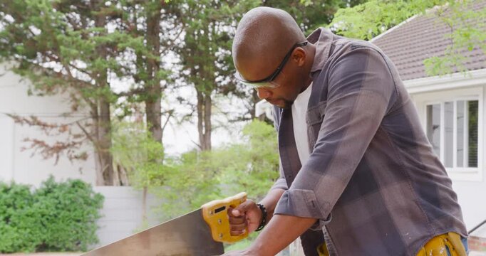 African American man sawing plank with yellow saw on yard bench, following mark, cutting to size