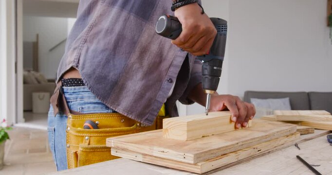 African American man placing block, aligning bit, using cordless drill on porch to fasten plywood