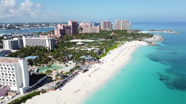 4K drone footage of a tropical beach in the Bahamas featuring white sand, turquoise water, palm trees, and seaside resorts. Bright sunshine and clear blue sky create a perfect vacation destination sce
