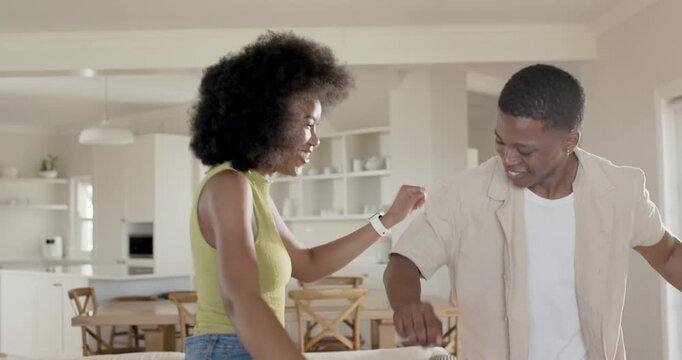 African American couple dancing playfully in bright home by sofa while woman tapping man's head