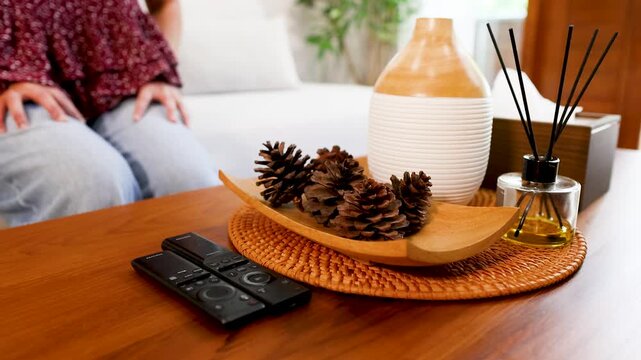 Woman Reaching for a Television Remote Control on a Living Room Table