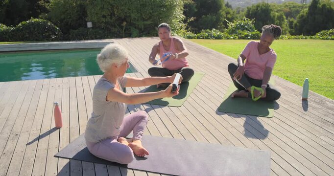 Diverse women following senior turning picking band pulling overhead for tone on pool deck