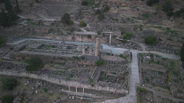 Aerial drone orbit shot around the Temple of Apollo ruins in Delphi, Greece at sunset, showcasing ancient archaeological landmark.