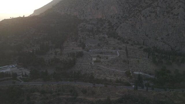 Aerial drone pull back reveal shot of the Temple of Apollo ruins in Delphi, Greece at sunset.
