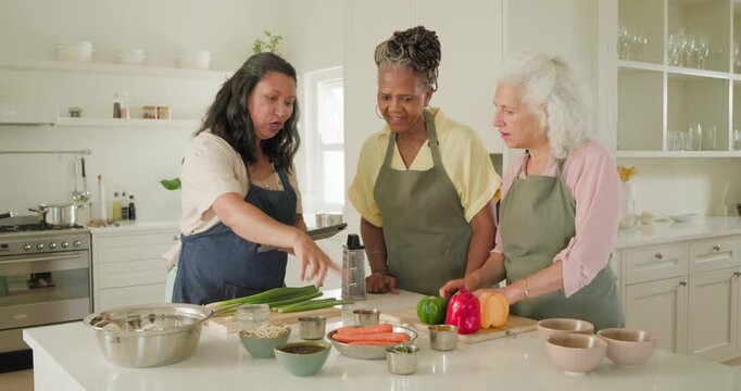 Diverse female friends consulting tablet and following recipe at kitchen island, slicing peppers