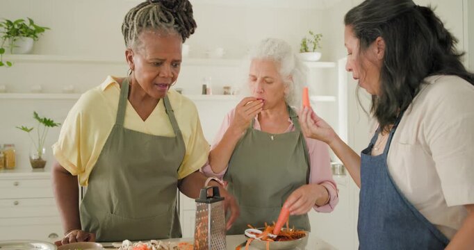 Diverse women in aprons after left woman's gasp peeling carrot and grating on grater prepping