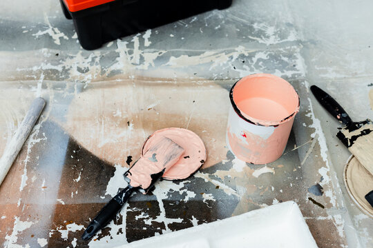 Open paint can sitting on cloth in renovation workspace, putty knife resting on lid, brush drying