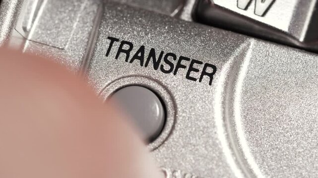 Macro close up of transfer button pressed on metallic silver panel with black lettering