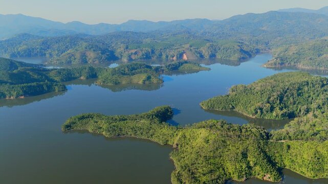 Aerial drone view of Buon Me Thuot in Dak Lak showing calm lake, forested hills, and layered mountains forming scenic natural landscape under clear daylight sky