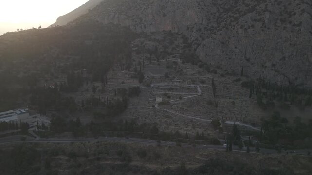 Aerial drone pull back reveal shot of the Temple of Apollo ruins in Delphi, Greece at sunset.