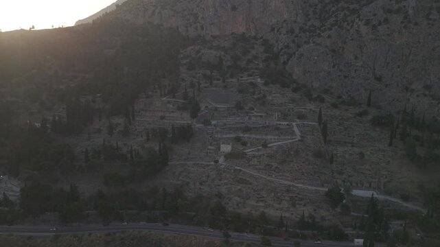 Aerial drone pull back reveal shot of the Temple of Apollo ruins in Delphi, Greece at sunset.