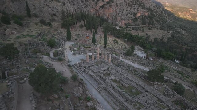 Aerial drone orbit shot around the Temple of Apollo ruins in Delphi, Greece at sunset, showcasing ancient archaeological landmark.