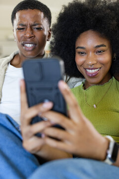 African American couple smiling, leaning in and studying smartphone with bulky case and pendant