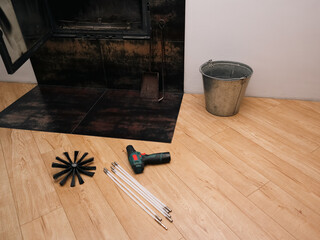 Chimney cleaning kit with brush rods and electric drill on wooden floor near fireplace, maintenance concept