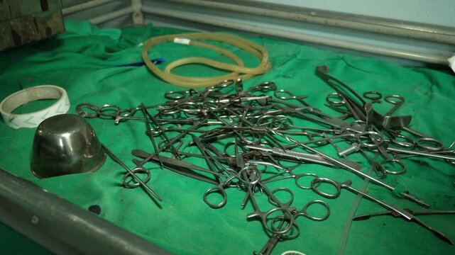 Metal surgical scissors and forceps piled on a green medical cloth in an outdated hospital in Cameroon. High angle view.