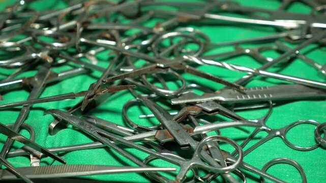 Metallic surgical tools piled on a green medical sheet in a rural Cameroonian hospital facility. Static shot.