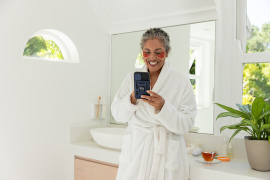 Smartphone is resting on vanity with under-eye gel patches, cup of tea, potted plant