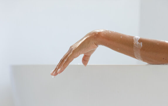Right forearm and hand resting on tub rim, lather, droplet forming on finger, falling, showing wash