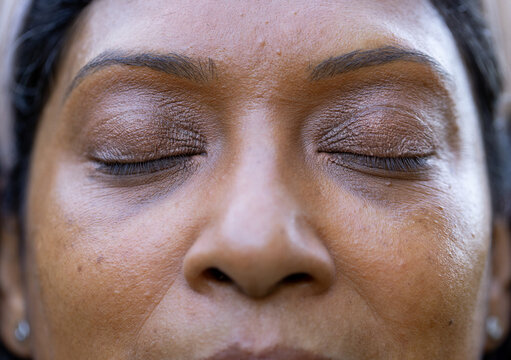 Indian woman closing eyes while showing brown metallic eyeshadow, mascara, stud earrings in studio