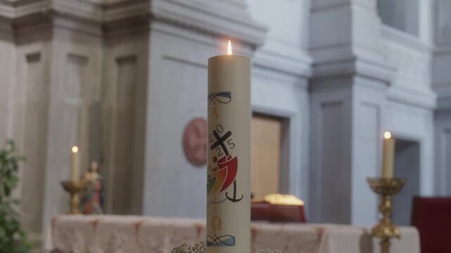 Close up of a lit decorated paschal candle burning brightly on an altar inside a blurred church background.