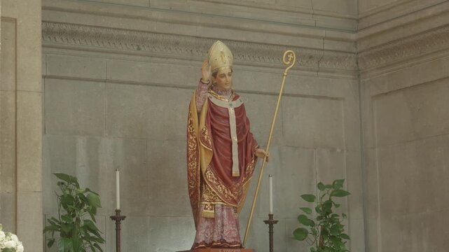 Religious statue of a Catholic bishop saint wearing traditional vestments and holding a golden crozier inside a stone church.