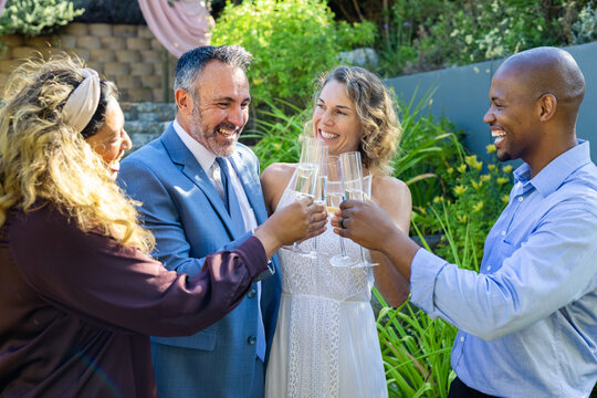 Diverse group toasting champagne flutes, celebrating couple in garden in blue suit and lace dress