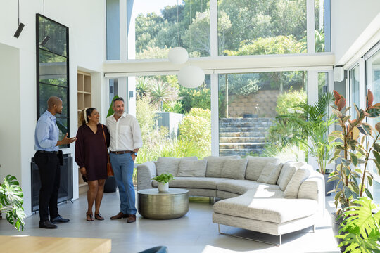 Diverse couple talking to African American agent showing glass walls and sectional sofa