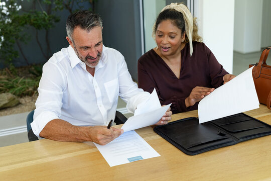 Receiving pages, two partners sitting at table reviewing, signing and closing contract by window