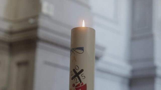 Extreme close up view of a burning decorated paschal candle featuring a cross symbol inside a bright church with blurred background.