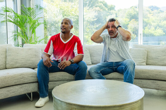 Vertical video: Watching men leaning in and holding heads at offscreen game in living room on sofa