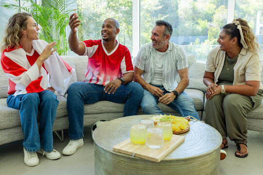 Raised hand starting conversation, four adults sitting on sofa gesturing, laughing, catching up