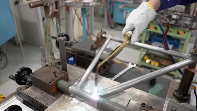 High angle shot of a technician using a blowtorch for precision brazing of a metal bicycle frame on an industrial jig