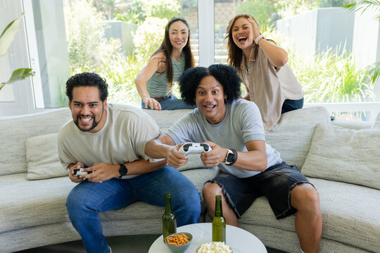 Friends gaming on sectional sofa in living room, holding white controllers, popcorn on coffee table