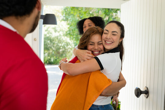 Diverse friends embracing and smiling at front door with orange blanket, door knob, bottles