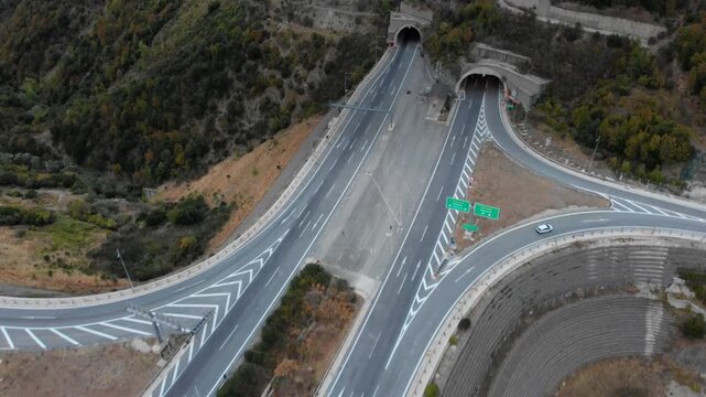 Aerial view of a highway interchange leading to tunnels through a mountain. Sparse traffic and lush greenery create a serene setting. Ideal for infrastructure and travel themes.