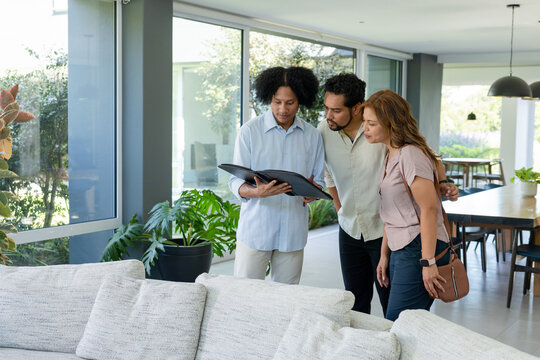 African American couple with male agent reviewing black portfolio near light sofa, potted plants