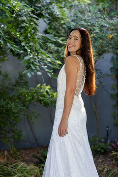 Adult woman standing in garden wearing white embroidered gown showing sheer floral back and ring