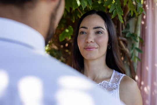 Couple standing, woman facing man in garden by vines and pink curtain, wearing white lace top