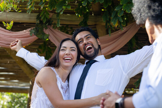 Romantic couple in white dress black tie hugging under pergola with pink drapes, guest shaking hand