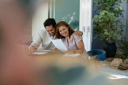 African American couple reviewing papers with pen, folder sitting at table near sliding glass door