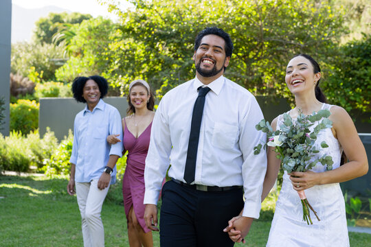 Couple walking hand-in-hand across garden lawn, bride wearing wedding dress holding bridal bouquet