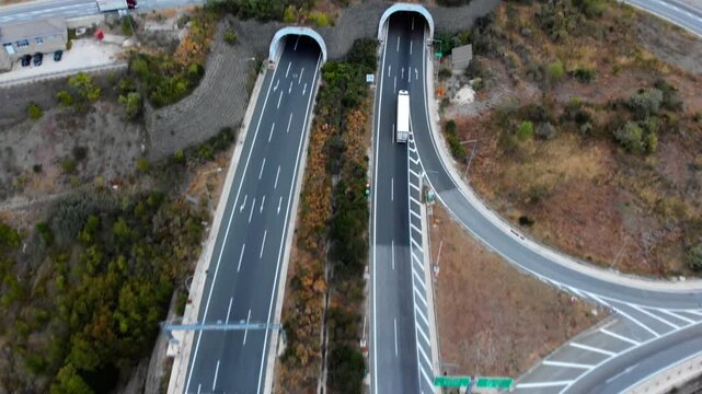 Aerial view of a truck approaching twin tunnels on the Egnatia Highway, surrounded by rugged mountain landscape. Ideal for transportation and infrastructure projects.